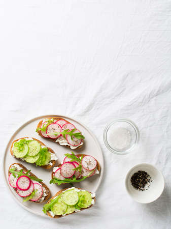 Some radish and cucumber toasts with ricotta and salad on white background wiht paper and saltの写真素材