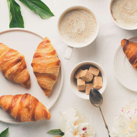 Breakfast on white flat lay. Croissants with cup of coffee and flowers