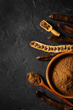 Carob bean and powder in bowl flat lay on black background, top view, copy space, verticalの写真素材