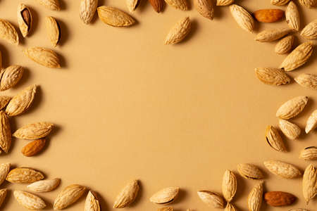 Almonds nuts with shell frame flat lay on brown background, layout, copy space
