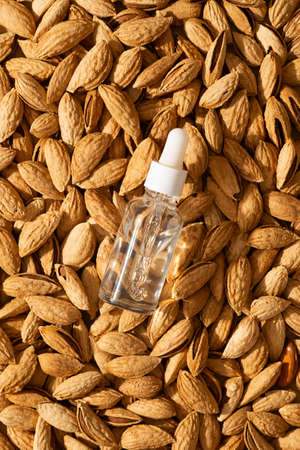 Essential almond oil and serum bottles nuts almonds with shell on beige or yellow background, top...