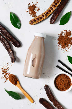 Carob drinks in bottle and carob beans, powder on white background, top view, verticalの写真素材