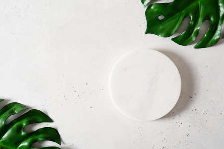 White cosmetic background with stone empty space platform and tropical leaf, flat layの写真素材
