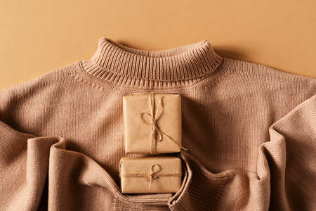 Eco friendly craft gift box with cozy sweater on brown background, top view, copy space, flat lay