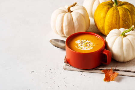 Autumn pumpkin soup in red or orange bowl with vegetablesの写真素材