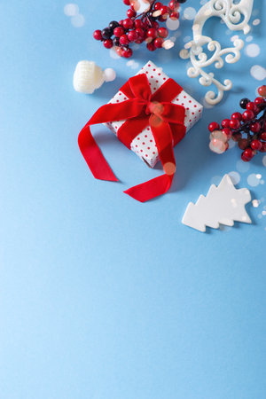 Christmas and happy new year card border with gift box, red berries branch and white toy on blue background, flat lay, top view, copy space, verticalの写真素材