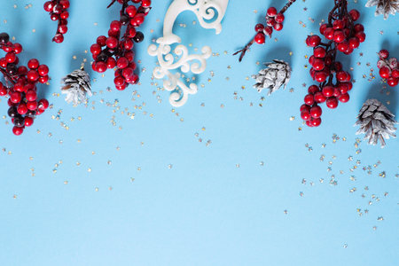 Christmas and happy new year card border with red berries branch and toy on blue background, flat lay, top view, copy spaceの写真素材