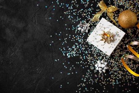 Christmas and happy new year card with box and gold bow, ball and shimmer on black background