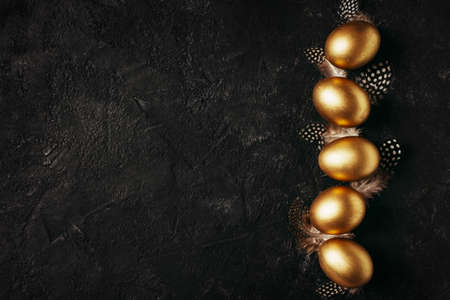 Happy easter concept flat lay with gold eggs and feather on black backgroundの写真素材