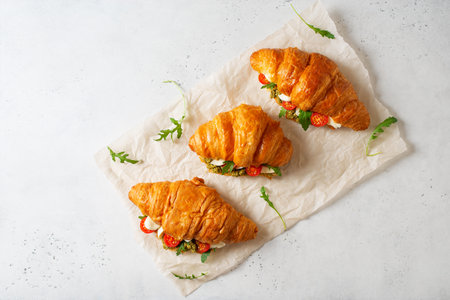 Three croissants with cheese, tomato, pesto and arugula on white backgroundの写真素材
