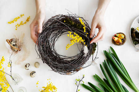 Easter wreath diy with woman hands, flowers on table, handicraft