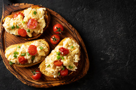 Scrambled eggs with onion and tomatoes on grilled toasts on black background