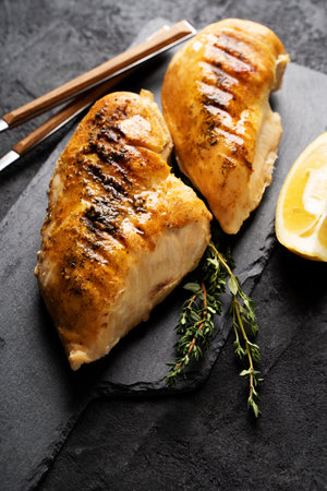 Chicken grilled steak breast on board with tableware on black background, copy space, top view, verticalの写真素材