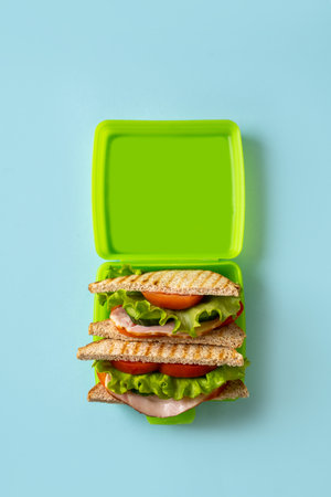 Sandwich toast with fresh salad, tomato, ham in lunchbox on blue background, copy space, verticalの写真素材