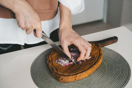 Woman hands cutting onion on wooden board close up indoor, home cooking lifestyleの写真素材