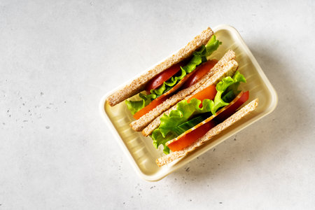 Sandwich toast with fresh salad, tomato, bacon in lunch box, top view on white background, copy spaceの写真素材