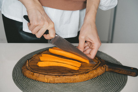 Woman hands cutting carrot on wooden board close up indoor, home cooking lifestyle