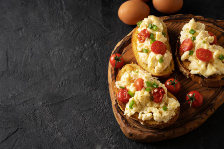 Scrambled eggs with onion and tomatoes on grilled toasts on black background