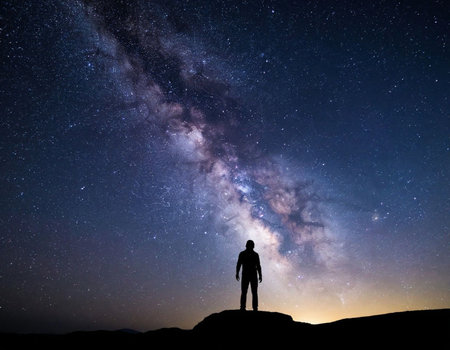 Silhouette of a man standing on top of a mountain and looking at the milky way galaxy.