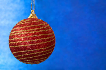 Red Christmas toy with gold stripes on a blue background close-up. New Year, christmas background.                               の写真素材