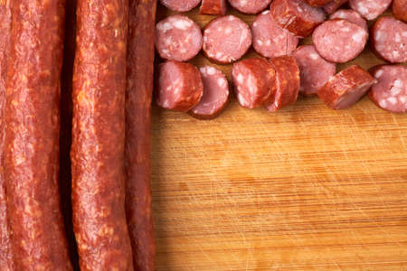 Thin smoked sausage whole and sliced on a wooden background.