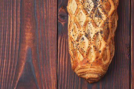 Baked bun with flaky pastry sprinkled with poppy seeds on a dark wooden background. Close-up. Food background.の写真素材