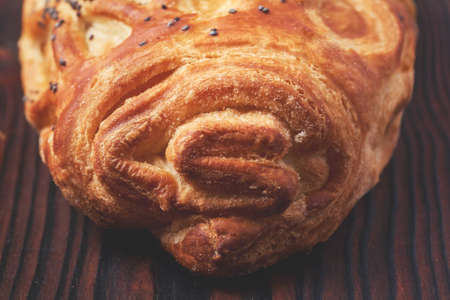 Baked bun with flaky pastry sprinkled with poppy seeds on a dark wooden background. Close-up. Food background.の写真素材