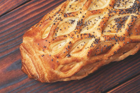 Baked bun with flaky pastry sprinkled with poppy seeds on a dark wooden background. Close-up. Food background.の写真素材