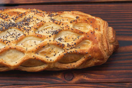 Baked bun with flaky pastry sprinkled with poppy seeds on a dark wooden background. Close-up. Food background.の写真素材