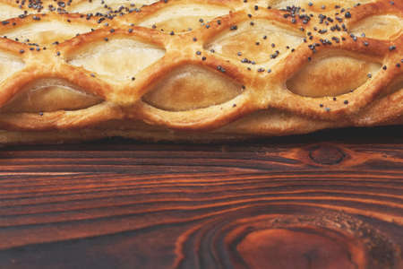 Baked bun with flaky pastry sprinkled with poppy seeds on a dark wooden background. Close-up. Food...
