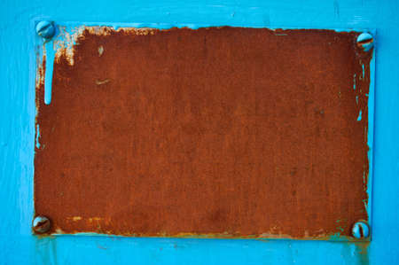 Rusty metal plate bolted with four bolts on a blue background. Abstract background.
