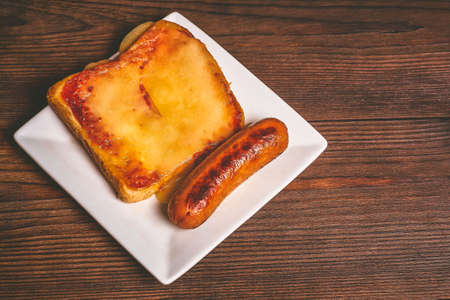 Sandwich with melted cheese and grilled sausages closeup on a dark wooden background.の写真素材