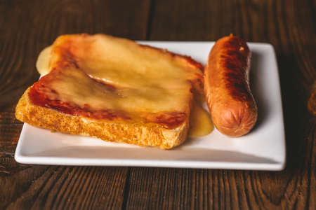 Sandwich with melted cheese and grilled sausages closeup on a dark wooden background.の写真素材