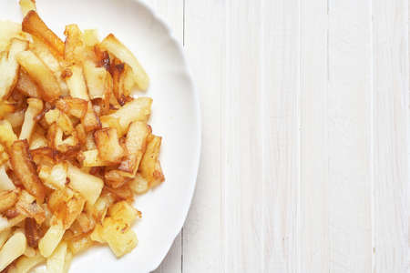 Fried potatoes in a white plate on a light wooden background.の写真素材