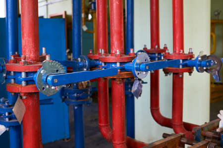 Blue valve on the hot water pipe is colored red. Industrial background.