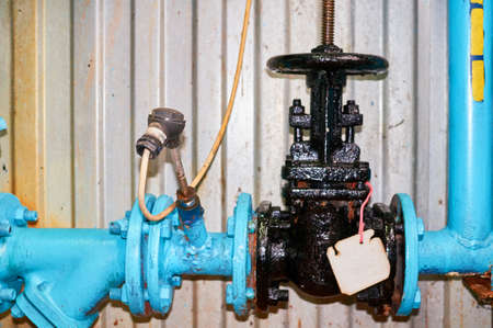 Old black valve on the cold water pipeline painted in blue. Industrial background.