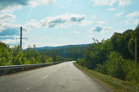 An asphalt road on the background of the forest and mountains.