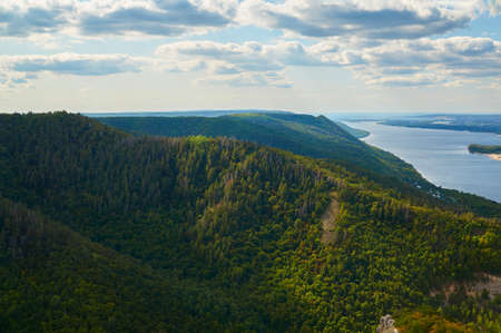 River against the blue sky with clouds and forests.