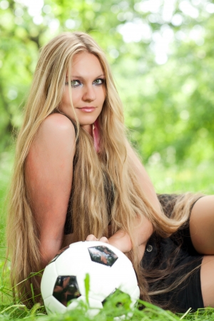 Girl sitting on the grass next to the soccer ball  beautiful young woman with long hair sitting around a soccer ballの写真素材