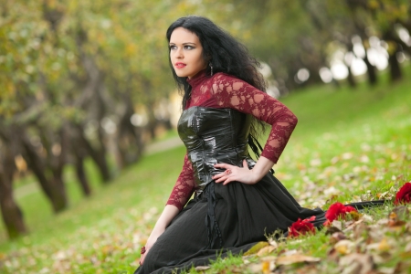 Beautiful gothic girl sitting on the grass in the autumn parkの写真素材