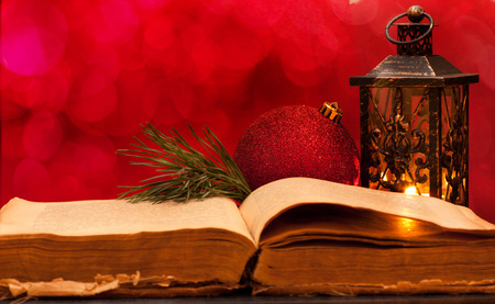 Open ancient Bible and Christmas decorations on a red background with bokehの写真素材