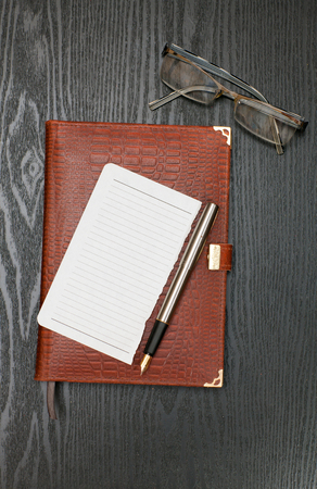 note, diary, pen and glasses lying on a black wooden tableの写真素材