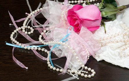 Beautiful pink rose, pearl beads and white stockings with garter lying on a tableの写真素材