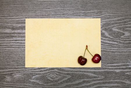 Cherry on the old yellow piece of paper on a wooden tableの写真素材