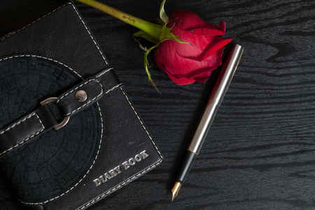 Diary book, pen and rose on a table of black woodの写真素材