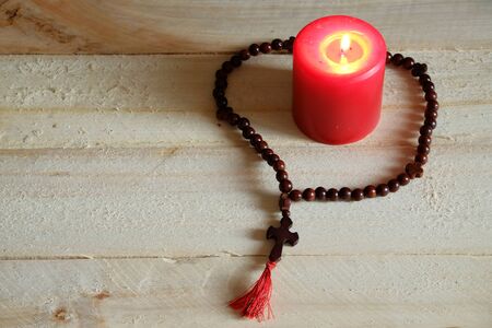 Rosary with a cross and a candle on a wooden tableの写真素材