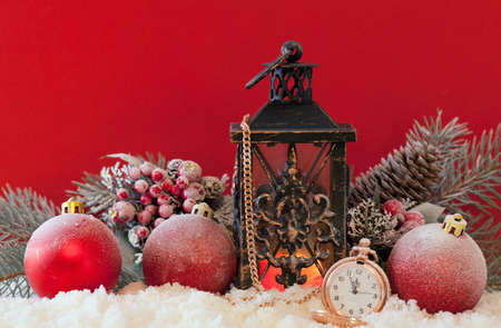 Candle lantern, christmas balls and pocket watch in the snow with a red background