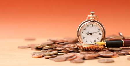 Pocket watch and coins on orange background closeupの写真素材