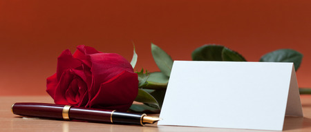 Red rose, sheet of paper and fountain pen lying on the tableの写真素材