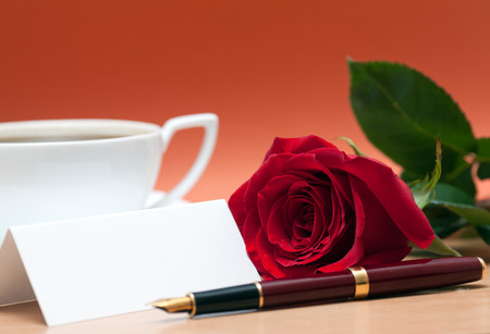 Red rose, cup of coffee, sheet of paper and fountain pen on the tableの写真素材